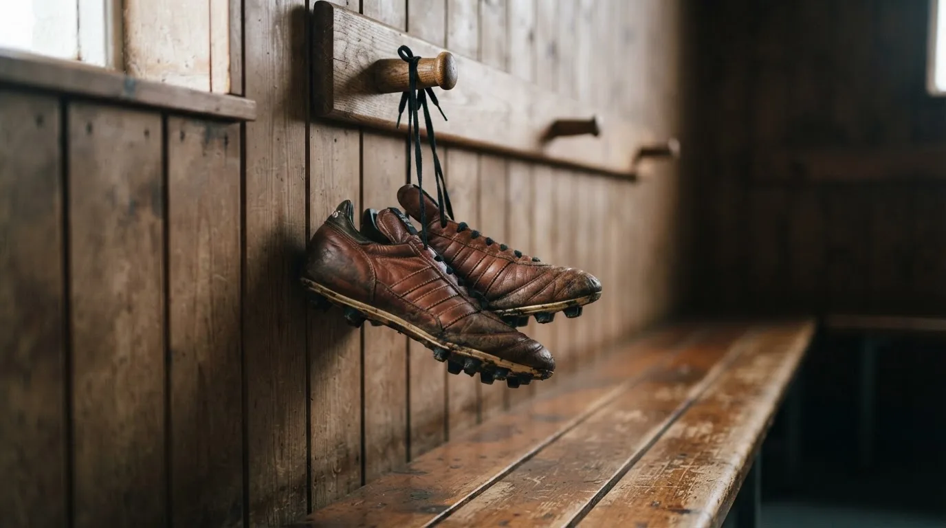 Ein Paar Fußballschuhe hängt an den Schnürsenkeln an einem Holzhaken in einer leeren Umkleidekabine.