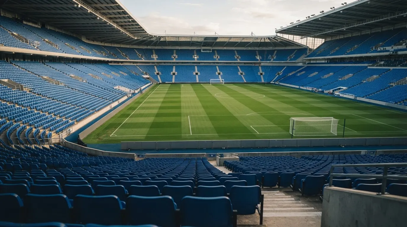 Ein leeres Fußballstadion bei Tageslicht von der Tribüne aus gesehen, der Rasen zeigt gleichmäßige Mähstreifen.