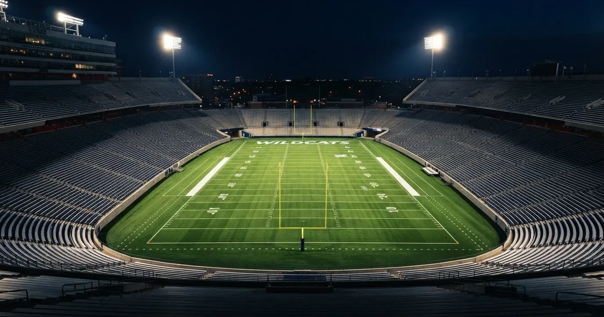 Ein American-Football-Feld mit weißen Yardlinien im Flutlicht, von einer hohen Tribüne aus gesehen, die Ränge leer, Zahlen nicht erkennbar.