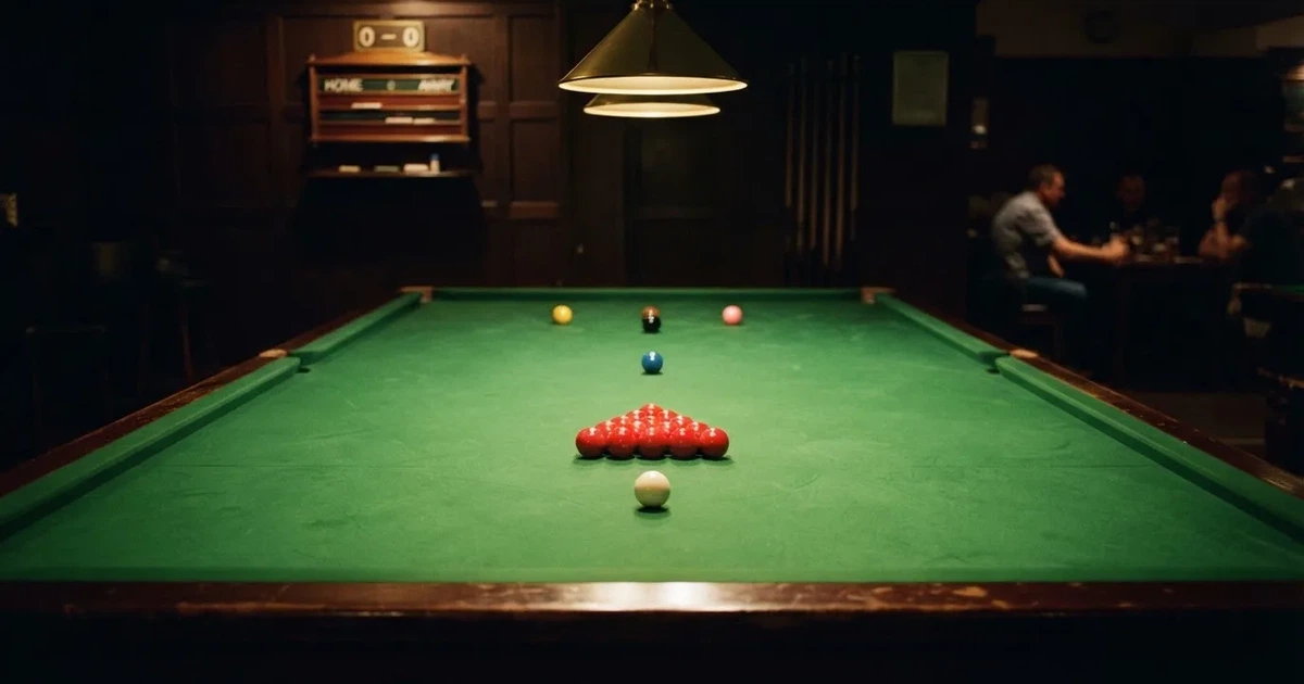 Ein Snookertisch mit grünem Tuch und aufgebauten roten Kugeln in einem abgedunkelten Raum unter einer hängenden Lampe.